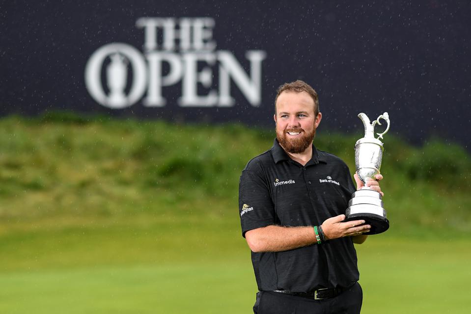 A smiling and standing man holding the british open cup